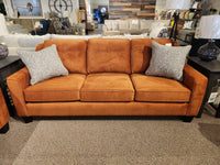 The showroom elegantly features the 4731 Sofa by Trendline, a Canadian-made three-seater in orange with a button-tufted back cushion and two patterned gray pillows.