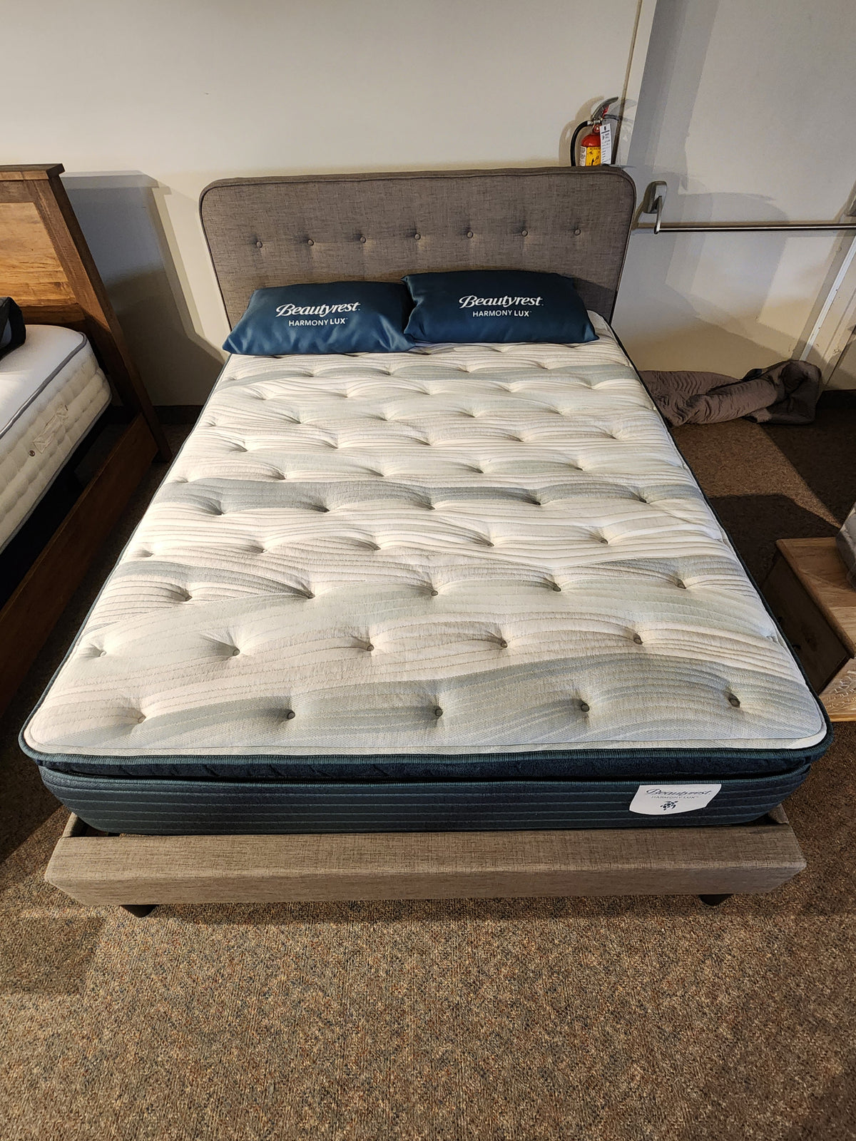 A neatly made bed with a Beauty-rest Glacier Grove mattress and two pillows on a wood frame in a showroom setting.