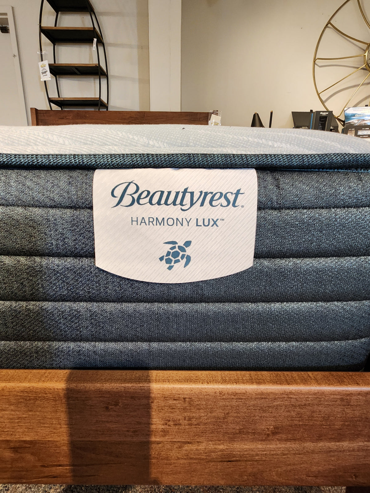 Close-up of a Beauty-rest Guava Gulf TT Firm Mattress in a showroom, showcasing the brand label and part of a wooden bed frame, promising firm support for restorative sleep.