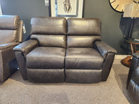 The La-Z-Boy 769-448 Ava Loveseat, a gray leather recliner, sits in a showroom against dark walls, artwork, a lamp, and clock.