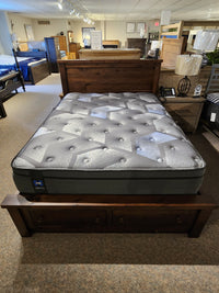 A Sealy Hunter ET Medium Mattress provides exceptional comfort and support on a queen-sized wooden bed frame with storage drawers, beautifully showcased in a furniture showroom.