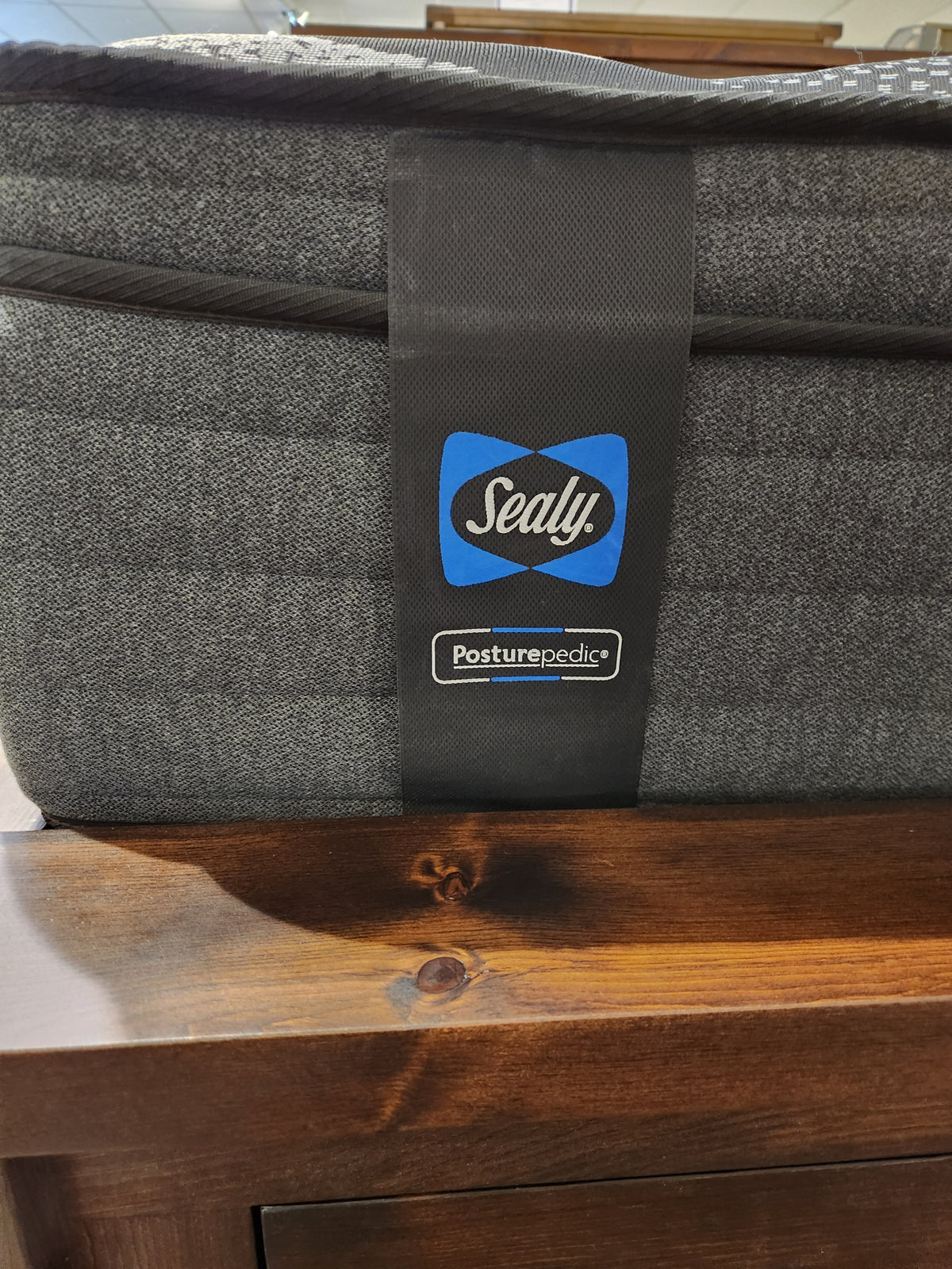 Close-up of a corner of the Sealy Joshua ET Soft Mattress with a logo tag, designed to offer a moisture-free sleeping experience. It is elegantly placed on a wooden surface, highlighting the exceptional comfort of its 800 Coil series.