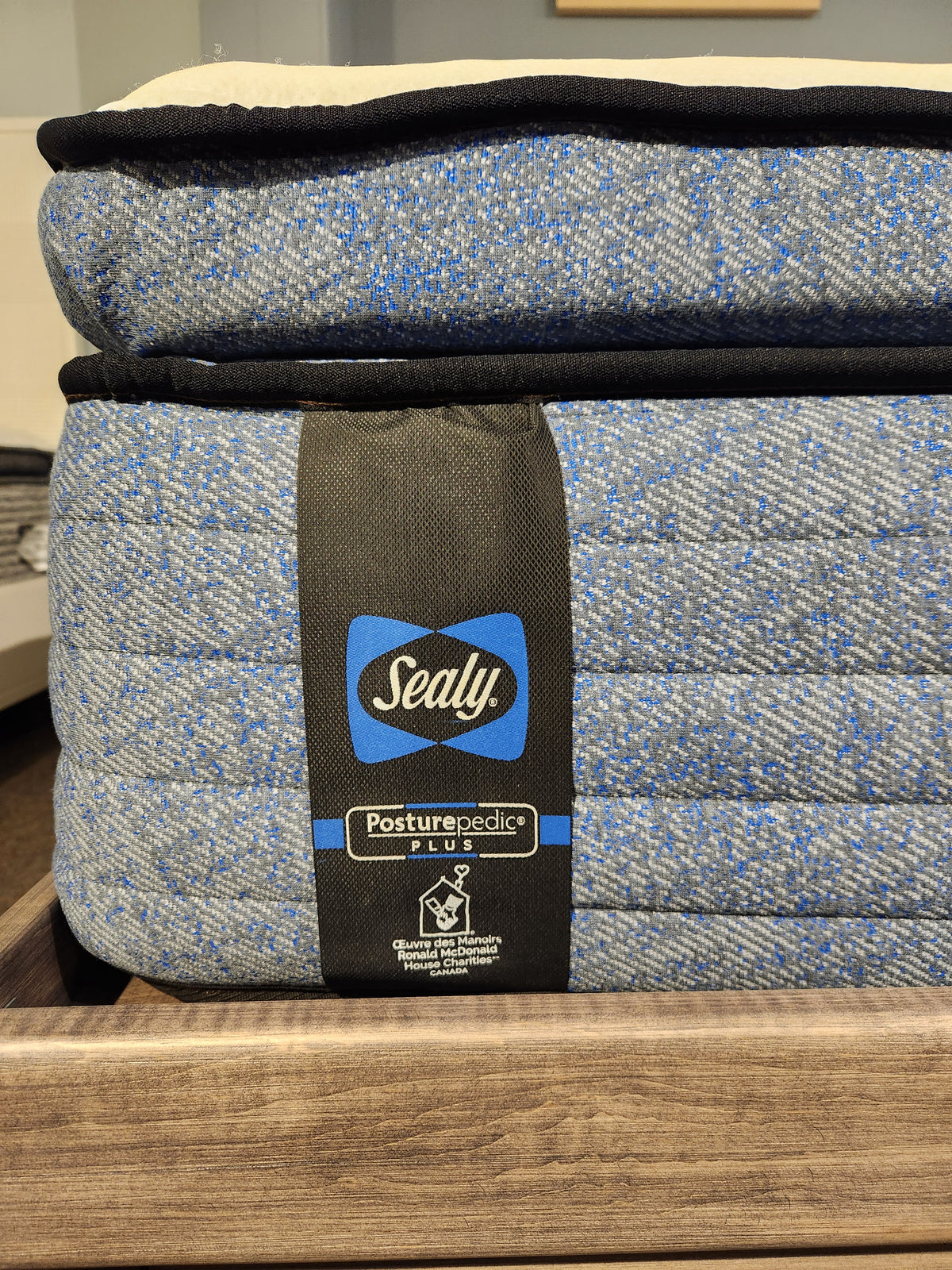 Close-up of a stacked Jacob ET Soft Mattress by Sealy with a "Posturepedic Plus" label, featuring a blue and gray patterned fabric. This Certipur-US certified product, showcasing its premium mattress quality, promises exceptional comfort and support with Sealy Comfort gel.