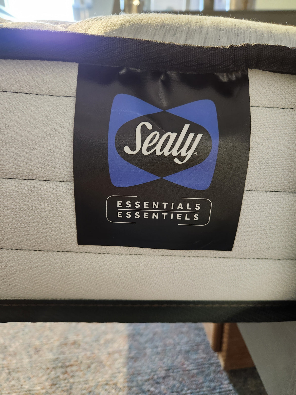 Label on the Alfie TT Medium Mattress, featuring the Sealy logo and brand name in a showroom environment, emphasizing its all-foam construction with Sealy Support HD Foam for maximum comfort.