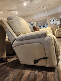 Side view of a La-z-boy 530 Greyson Wall-a-Way Recliner in beige, featuring a black handle and power recline option, displayed in a showroom with wooden flooring and a large clock on the wall.