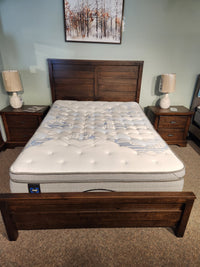 Queen-sized bed featuring a Sealy Sabine ET Soft Mattress crafted with Certipur-US certified materials. This elegant wooden frame and headboard are perfectly paired with two wooden nightstands topped with lamps to create a cozy ambiance.