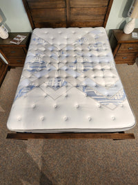 The Sealy Sabine ET Soft Mattress, which is Certipur-US certified, boasts a white and blue patterned cover placed on a wooden bed frame. The room's tranquil atmosphere is enhanced by the presence of two side tables with lamps.