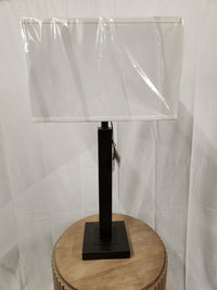 The Cooper Table Lamp by Pacific Coast, with a gunmetal finish and white shade, sits on a round wooden table.