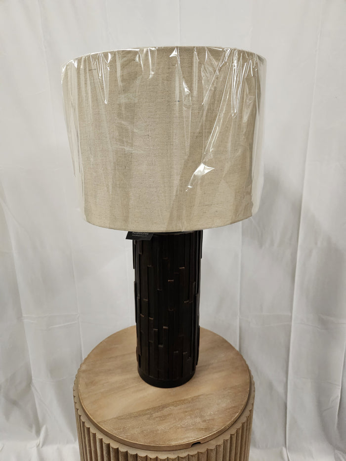 A round beige Ashley L243234 Makya Table Lamp with a wrapped shade stands on a wooden table against a white background.