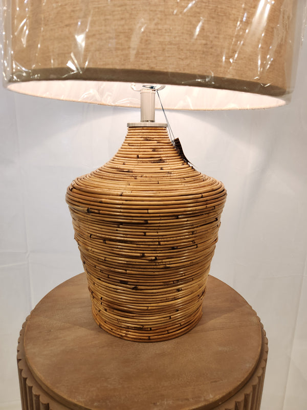 The Ashley L329034 Kerrus Table Lamp boasts a boho-chic woven rattan design with a beige shade on a wooden pedestal.