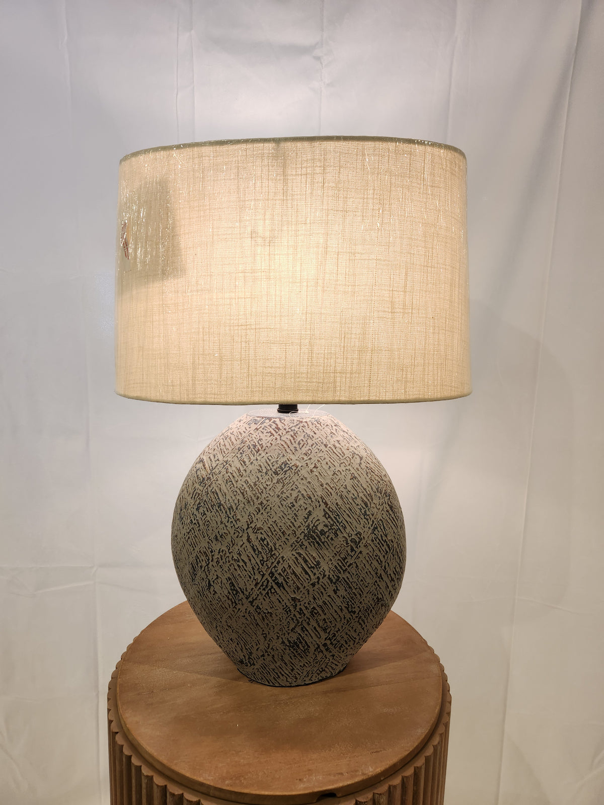 The Harif Paper L235624 Table Lamp by Ashley adds charm to decor with its textured base and beige shade on a wooden table.