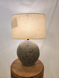 The Harif Paper L235624 Table Lamp by Ashley adds charm to decor with its textured base and beige shade on a wooden table.