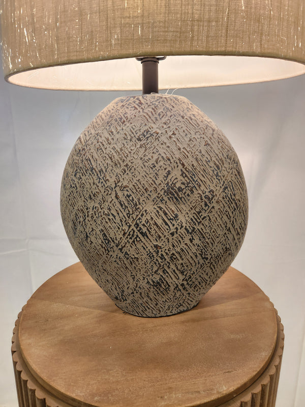 Ashley’s Harif Paper L235624 lamp, a home decor gem, boasts a textured base with beige shade on a wooden table.