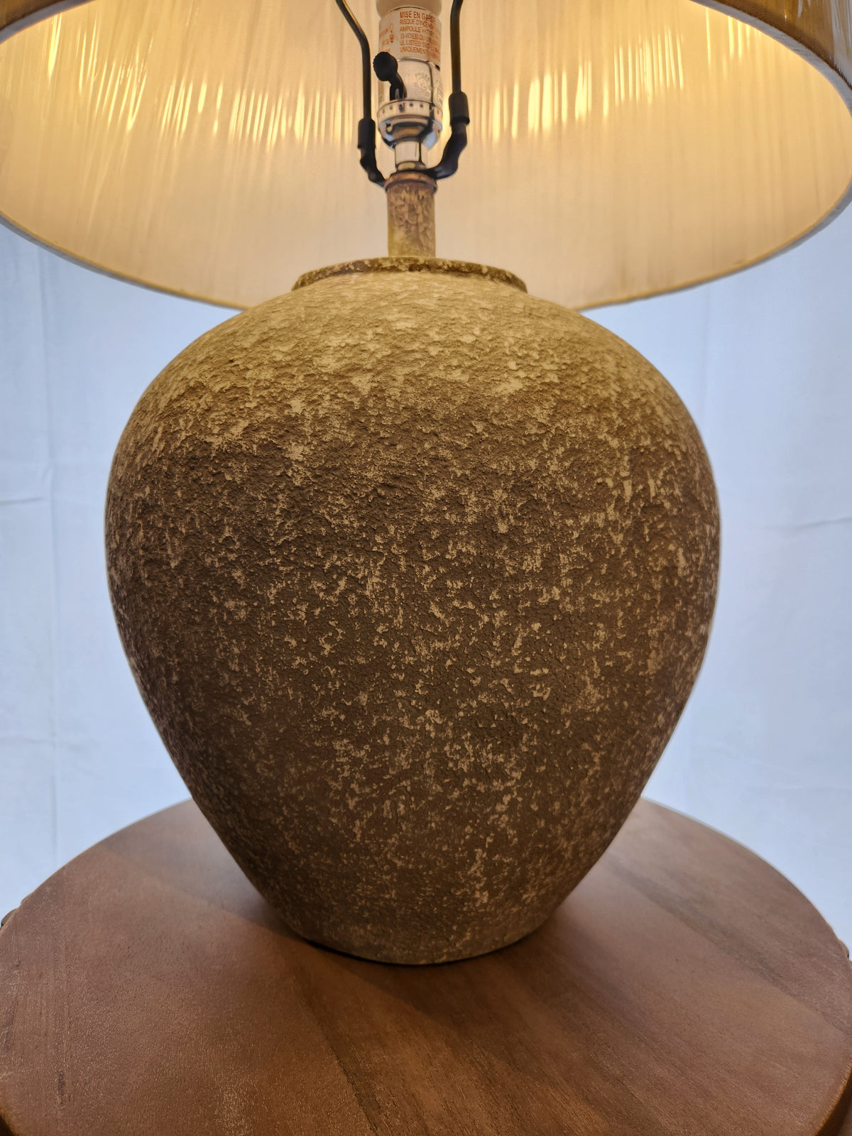 The Ashley Dreward Table Lamp with a distressed gray finish and beige shade sits on a wooden surface.