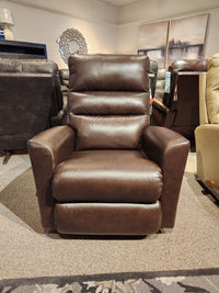 The 786 Liam Rocker Recliner from La-z-boy, featuring a casual style, is displayed in a showroom. Surrounded by other furniture pieces, this brown leather recliner offers comfort and relaxation for any living space.