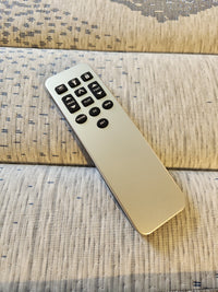 A remote control for the Essentials Adjustable Base by Fashion, featuring a sleek silver design with black buttons, is placed on a surface covered in light patterned fabric.