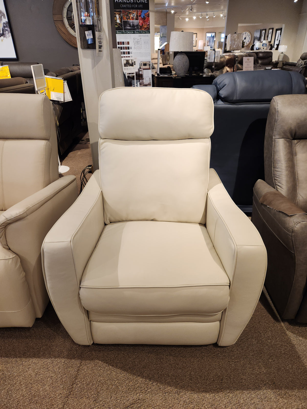 The Oakridge 40180-C1 Power Chair by Palliser, a cream-colored recliner featuring durable spring seats, is on display in a furniture store, showcasing its upscale appeal amidst an array of other chairs.