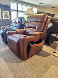 La-z-boy's Lay-Z-Boy 762-16X Neo Power Wall-a-Way Recliner, crafted from brown leather and featuring an adjustable headrest and a built-in side pocket, is showcased in a showroom setting under soft lighting near a window.