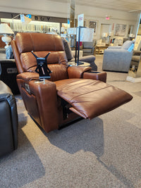 In the furniture store showroom, a La-Z-Boy 762-16X Neo Power Wall-a-Way Recliner in brown leather takes center stage. It features an adjustable headrest and a convenient tray table attachment, while other stylish chairs stand in the background, creating a welcoming ambiance.