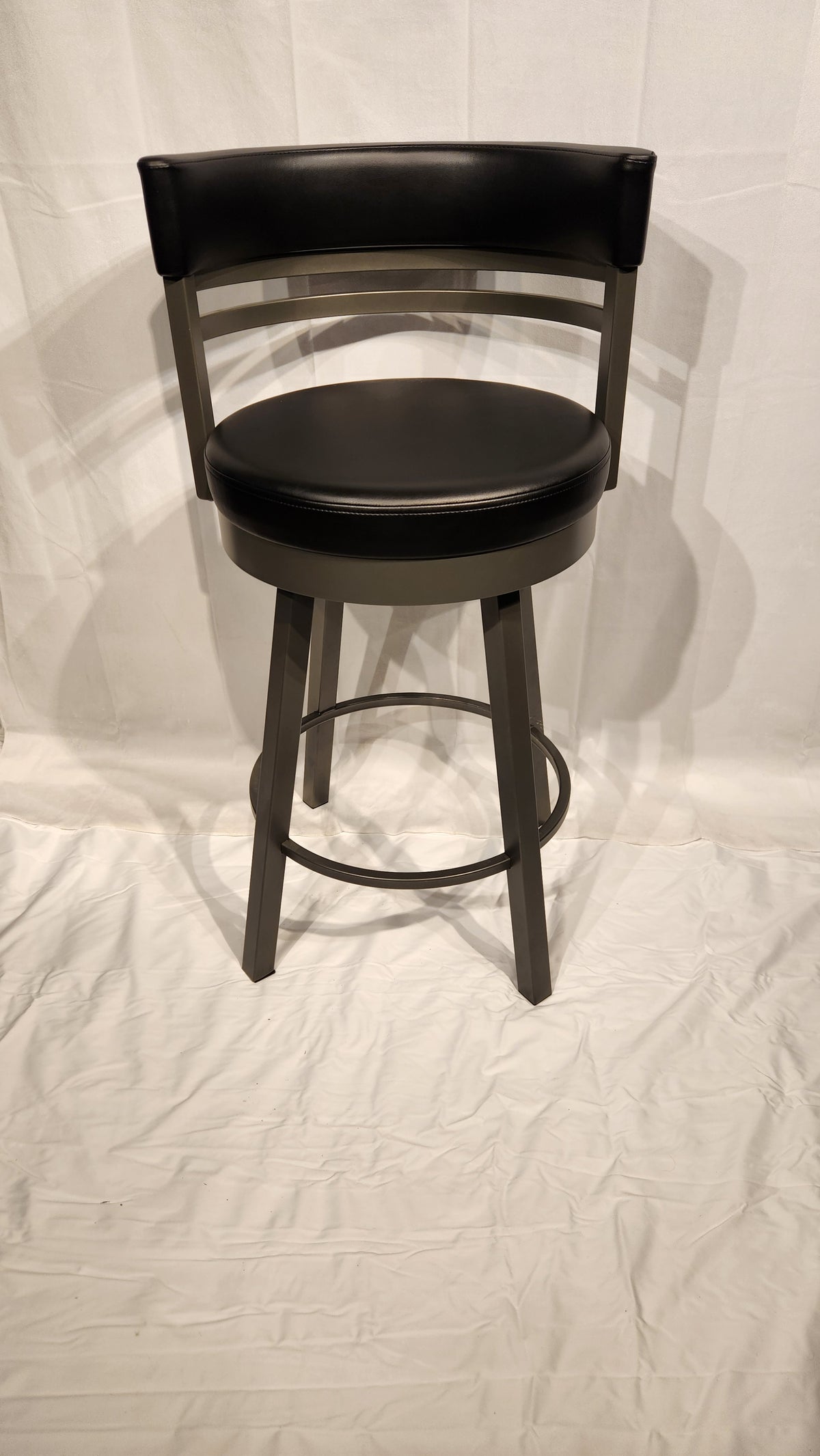 The Amisco Ronny Swivel Stool features a black cushioned seat and backrest on shiny metal, set against a white backdrop.