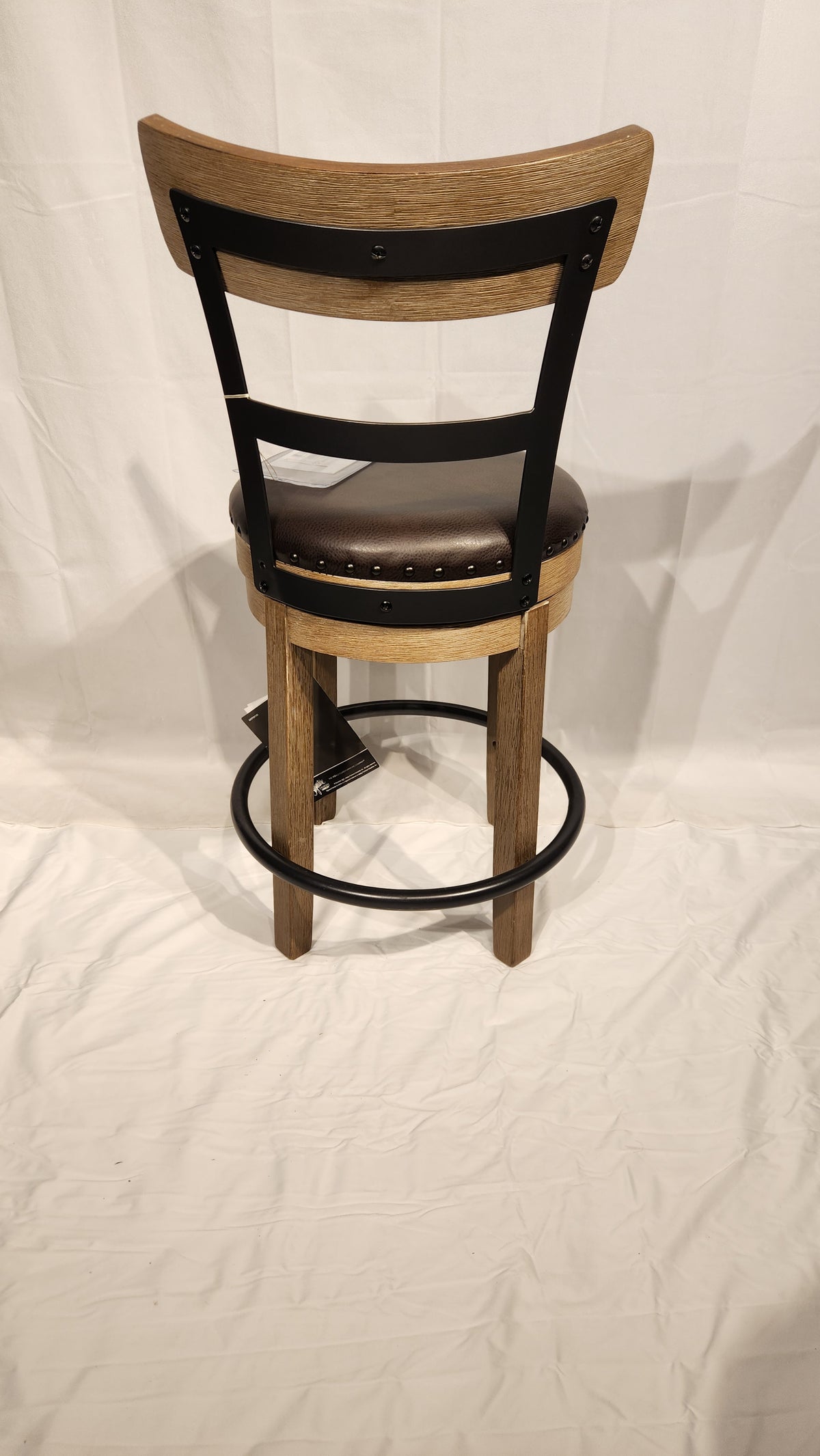 An Ashley D542 Pinnadel stool features a brown cushioned seat, black metal frame, and circular footrest on white fabric.