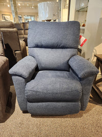 The 727 Brooks Rocker Recliner by La-Z-Boy, featuring a modern silhouette and cozy blue fabric, is showcased in a furniture showroom, providing unmatched comfort among an assortment of stylish pieces.