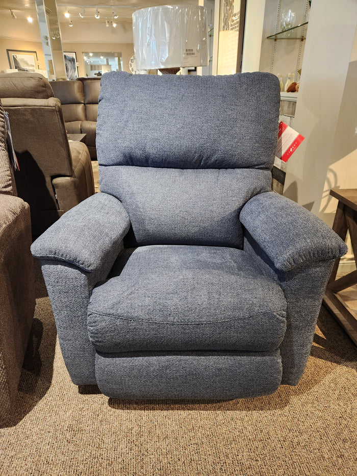 The 727 Brooks Rocker Recliner by La-Z-Boy, featuring a modern silhouette and cozy blue fabric, is showcased in a furniture showroom, providing unmatched comfort among an assortment of stylish pieces.