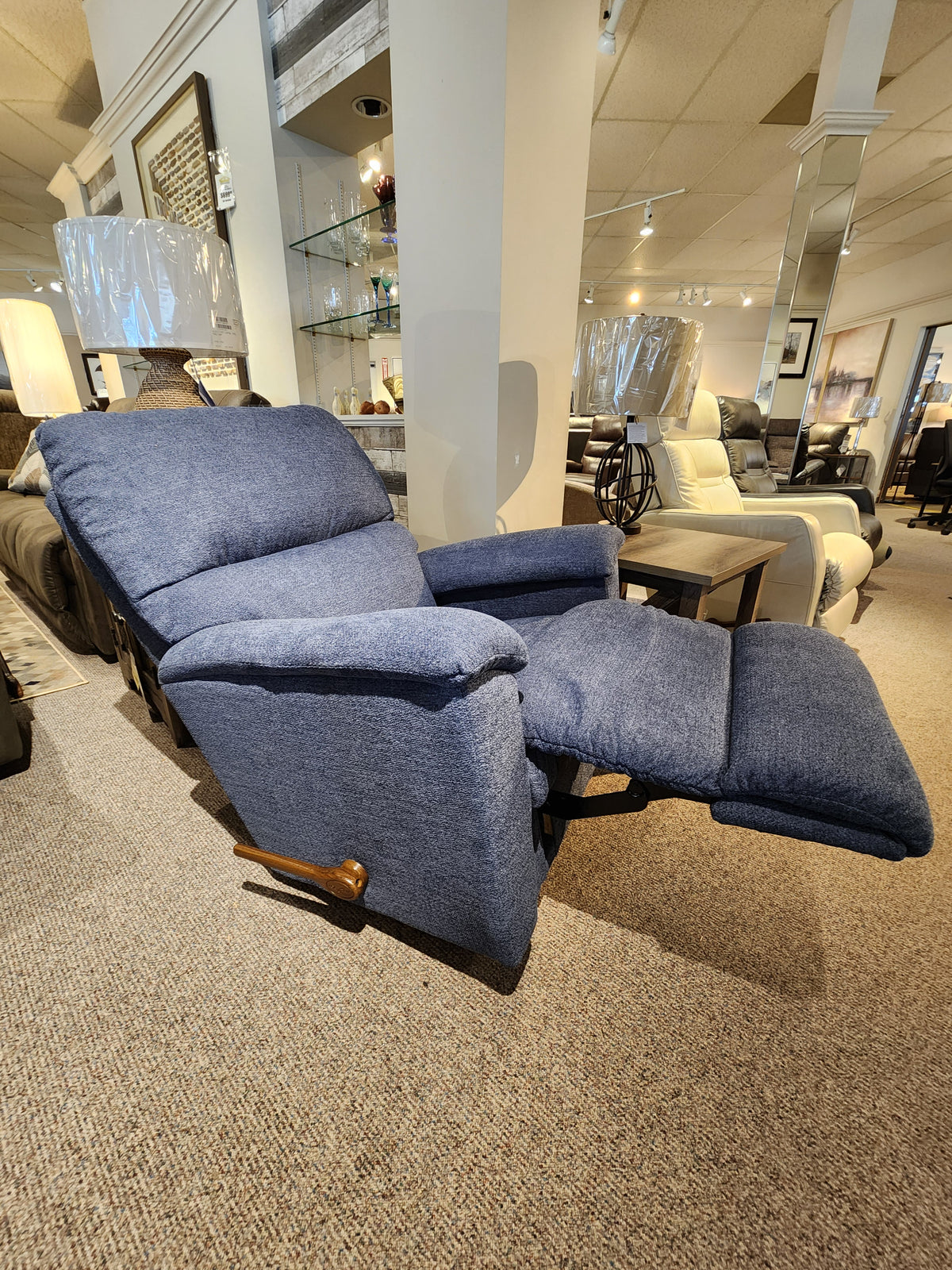 The La-z-boy 727 Brooks Rocker Recliner, featuring a modern silhouette, is a blue reclining chair showcased in the furniture showroom, offering unparalleled comfort amidst other chairs in the background.