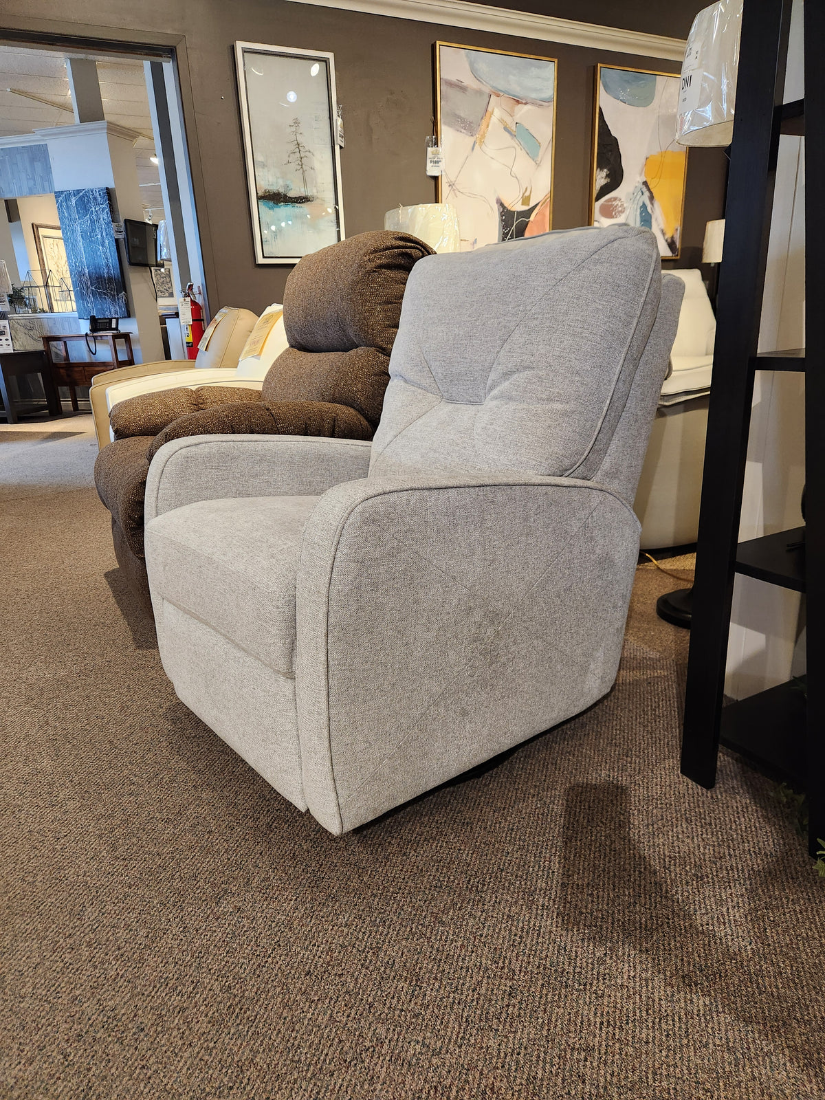 A Theo light gray Palliser Swivel Rocker Recliner with paintings behind it in a furniture showroom.