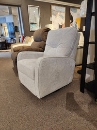 A Theo light gray Palliser Swivel Rocker Recliner with paintings behind it in a furniture showroom.