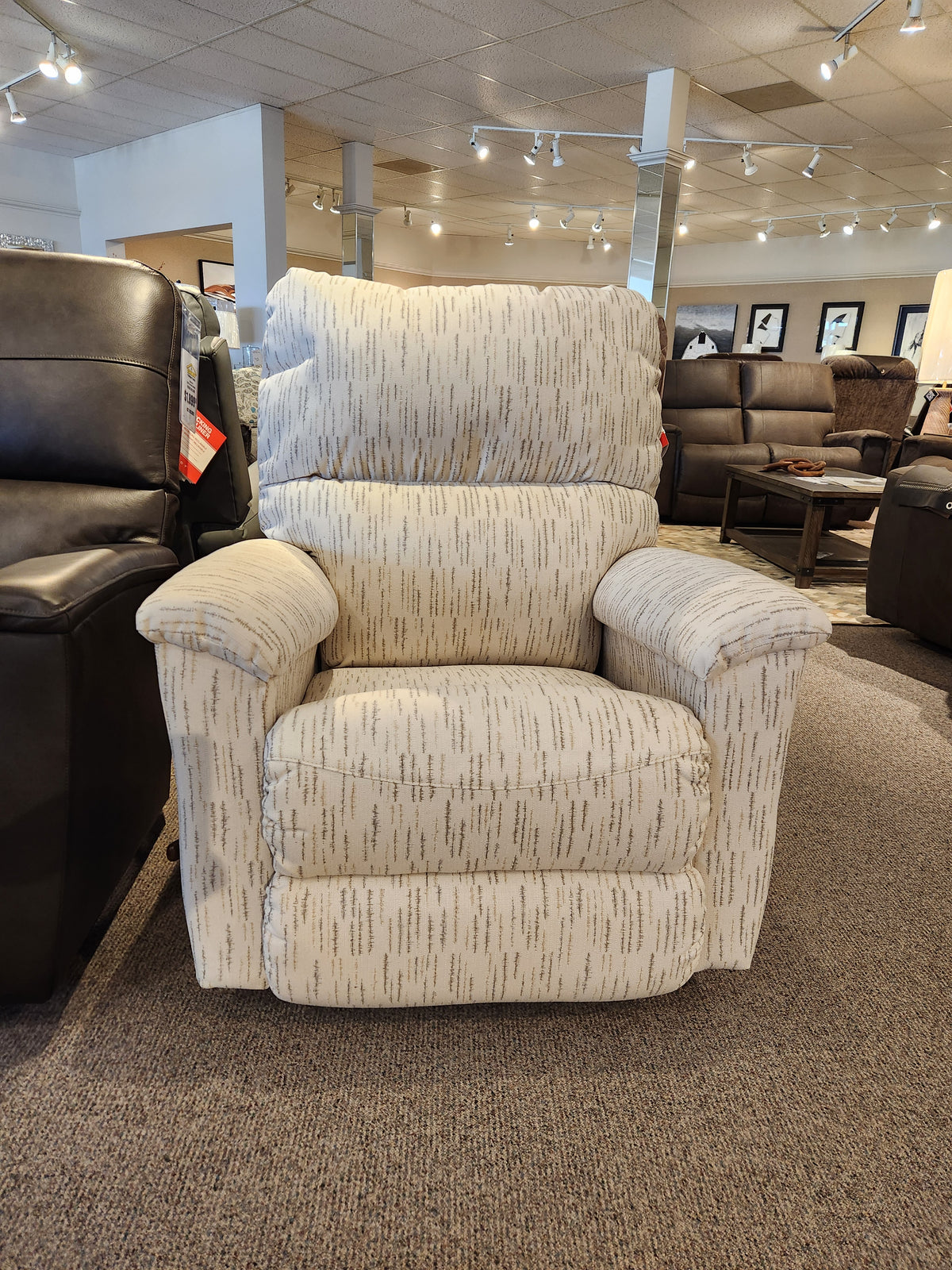 The La-Z-Boy 727 Brooks Rocker Recliner, featuring beige patterned upholstery, showcases a modern silhouette and provides unparalleled comfort in the furniture store showroom.