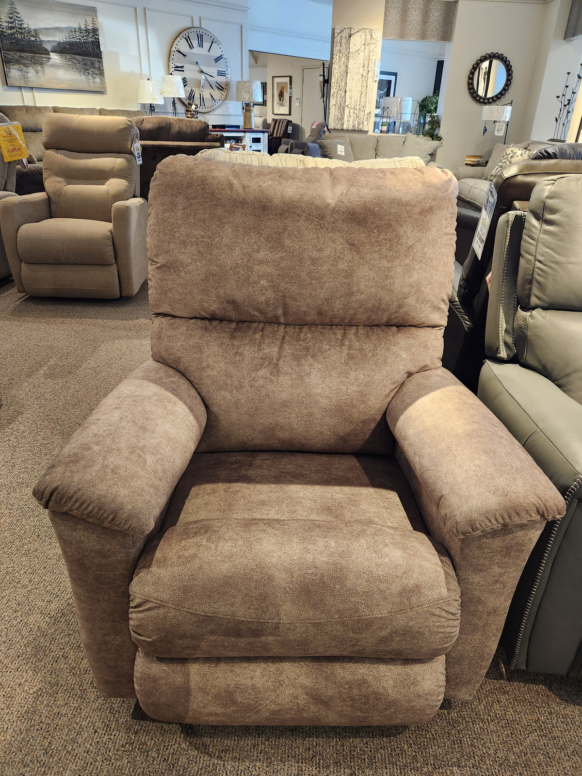 A brown 727 Brooks Rocker Recliner by La-Z-Boy is showcased in a furniture store, amidst a collection of other recliners and decorative pieces. Its modern design and exceptional comfort make it an appealing option for any living area.