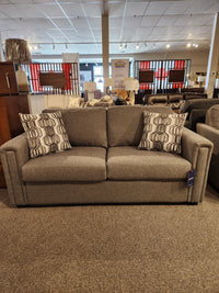 The Simmons Upholstery showroom is featuring the 9350 Double Sofa Bed, a gray fabric piece with sleek track arms and two patterned pillows.