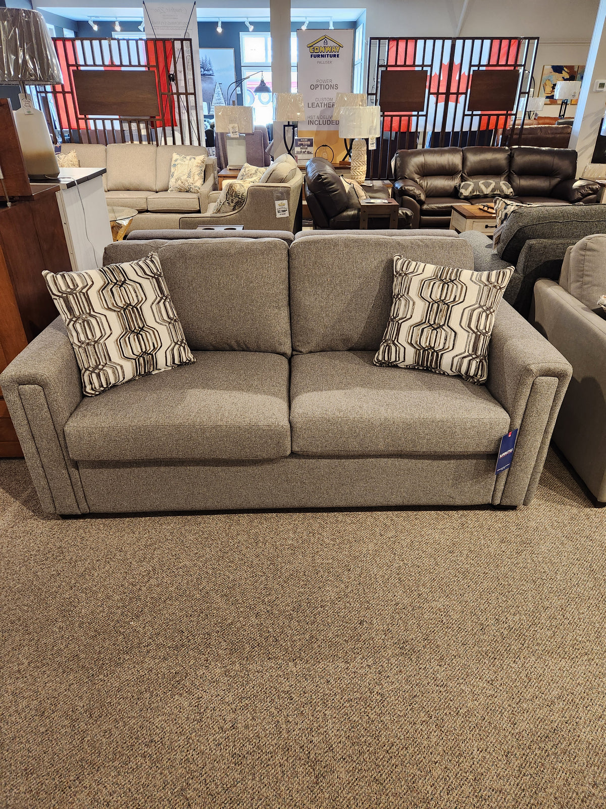 Simmons Upholstery's 9350 Double Sofa Bed, featuring track arms and two patterned pillows, is showcased in the furniture store showroom.