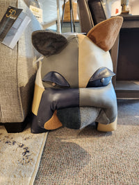 Reiner's Leather Animal Ottomans by Reiner's Originals feature a patchwork dog-shaped footstool, incorporating real leather accents and an assortment of fabric textures and colors. This unique design is displayed on a carpeted floor in a furniture store, emphasizing the charm of animal ottomans.