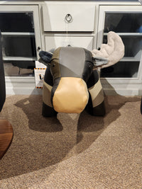 A creatively designed Reiner's Leather Animal Ottoman, shaped like a moose, enhances the carpeted area in front of a glass-doored cabinet, providing a playful touch to any room, courtesy of Reiner's Originals.