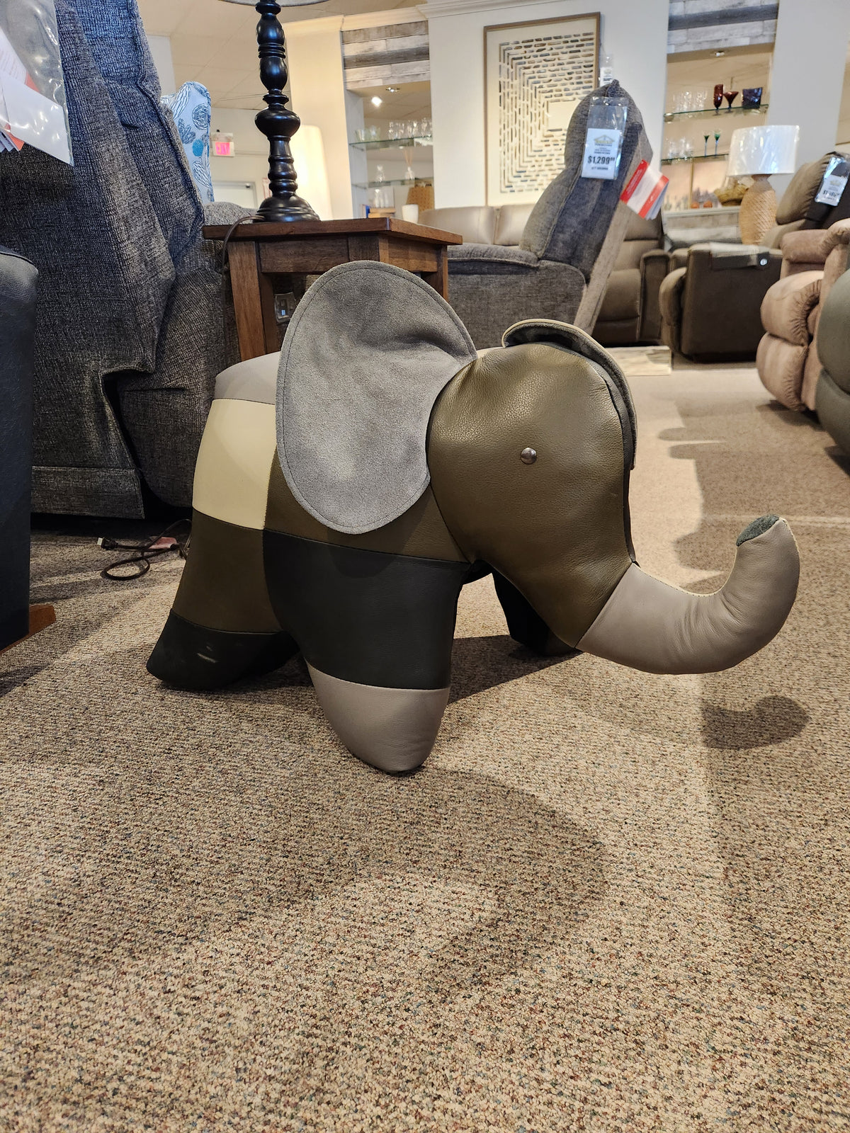 A Reiner's Originals leather animal ottoman, specifically designed as a patchwork elephant, is showcased on the carpeted floor of our showroom.