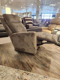 The La-z-boy 715 Kodie Rocker Recliner, made from gray corduroy fabric, stands as a centerpiece in the furniture store display. Surrounded by various seating options on the wood floor, it is designed for ultimate relaxation and invites you to unwind and enjoy its cozy embrace.