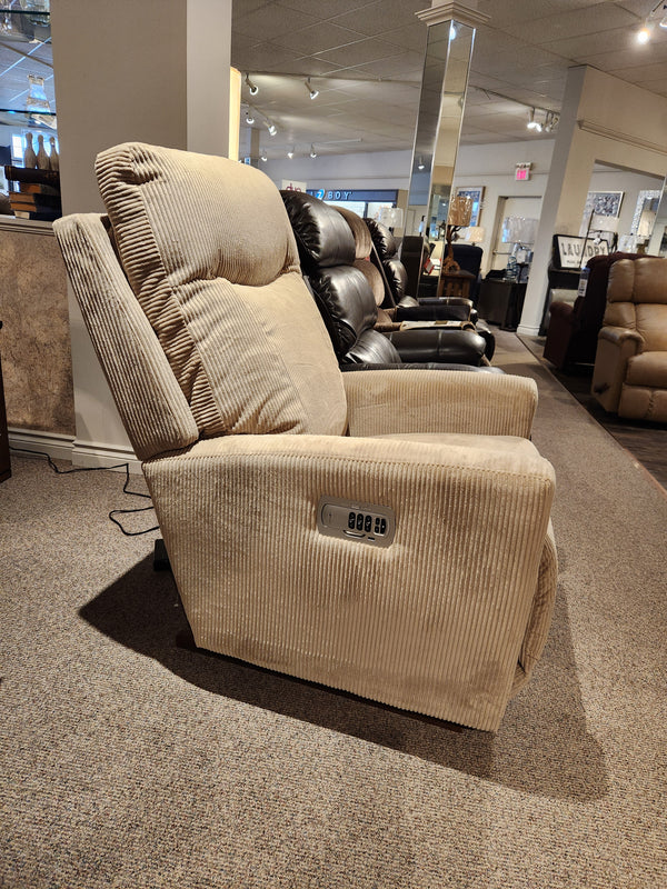 The La-z-boy 715 Kodie Rocker Recliner, draped in luxurious corduroy fabric, is displayed in a furniture store showroom. This beige chair comes equipped with a handy control panel on the side to ensure maximum comfort.