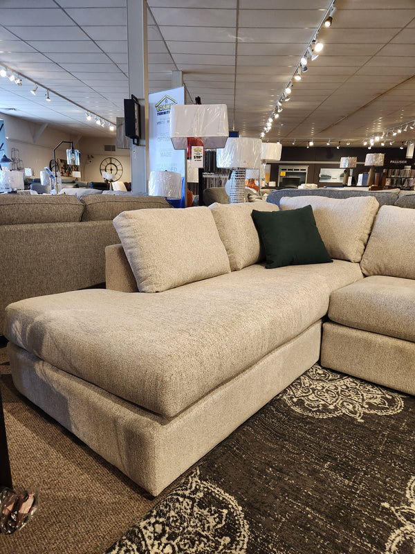 In a chic furniture showroom, the 2068 Malibu Sectional from Decor-rest is elegantly displayed with a green pillow. It's encircled by an assortment of lamps and decor, providing both comfort and sophistication with its high resiliency foam construction.