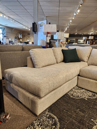 Part of Decor-rest's 2068 Malibu Sectional lineup, this beige sofa with a green pillow is featured in a furniture store, promising ultimate comfort with its high resiliency foam cushions.