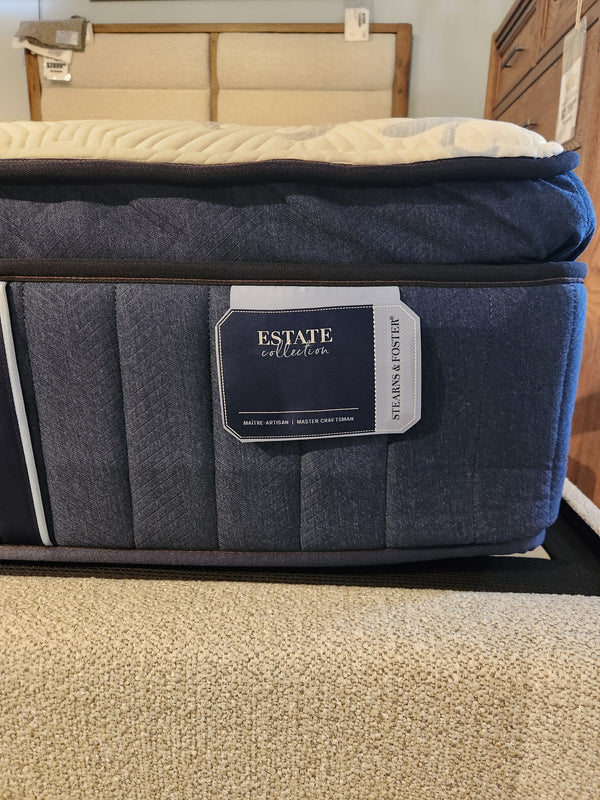 Close-up of a luxurious Amalia Pillow Top Cushion Firm Mattress from the Stearns & Foster brand, displayed in a store with a beige carpet visible in the foreground.