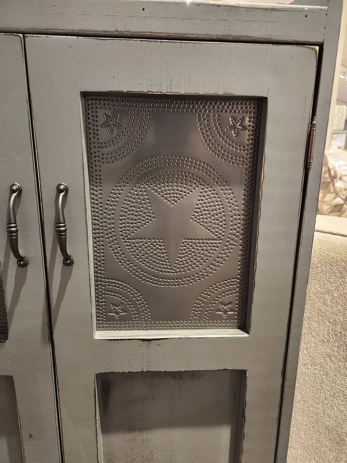 A detailed view of the 357 Punched Tin Cupboard by Woodcraft showcases Amish craftsmanship, adorned with decorative punched tin panels featuring star and circular patterns, complemented by metal handles.