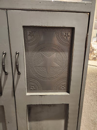 A detailed view of the 357 Punched Tin Cupboard by Woodcraft showcases Amish craftsmanship, adorned with decorative punched tin panels featuring star and circular patterns, complemented by metal handles.