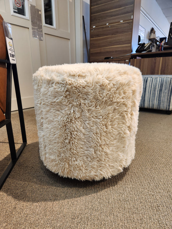 A Palliser 77004 Mingle Small Round Ottoman with single top stitching sits on a carpeted floor in a furniture store, offering the perfect furniture upgrade for any space.