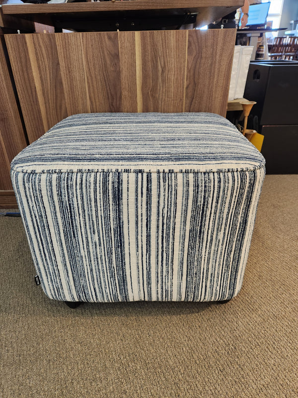 The 77004 Mingle Small Square Ottoman by Palliser has blue and white stripes and sits on a beige carpet with single top stitching.