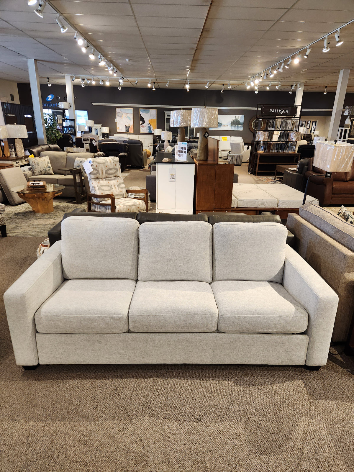 A Palliser 40526-22 Kildonan Queen Sofa Bed is displayed in beige with other furniture in the showroom.