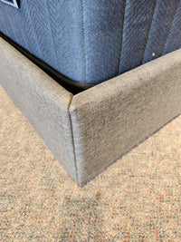 Close-up of a dark grey Donald Choi Alba Upholstered Bed Frame in queen size, resting gracefully on a beige carpeted floor.