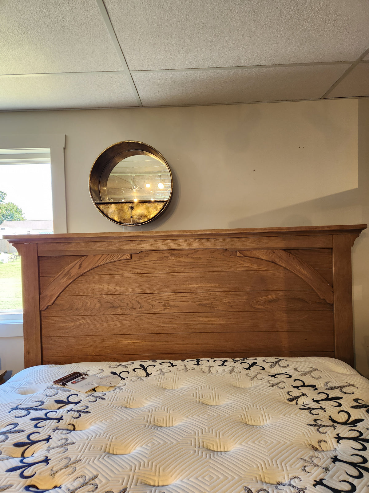 The 771 Vista Mansion King Storage Bed by Vaughan Bassett is beneath a round mirror on a beige wall, lit by daylight.