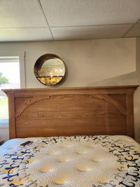 The 771 Vista Mansion King Storage Bed by Vaughan Bassett is beneath a round mirror on a beige wall, lit by daylight.